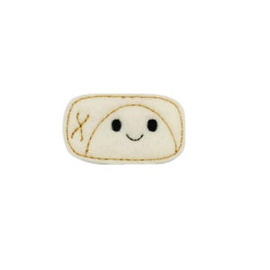 May include: A white felt patch with a smiling face and a gold embroidered outline. The face has two black eyes and a small mouth.