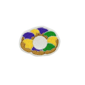 May include: A purple, green, and yellow embroidered patch shaped like a donut. The donut is outlined in brown.