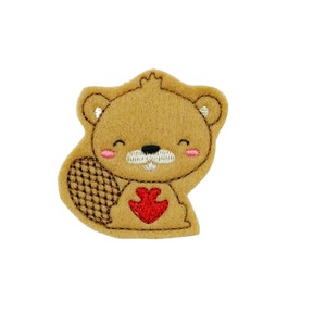 May include: A brown felt applique of a cartoon beaver with a red heart on its chest. The beaver has a white nose and mouth, and pink cheeks.