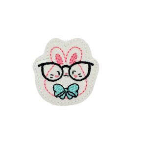 May include: White felt bunny with pink ears, wearing black framed glasses and a teal bow tie.