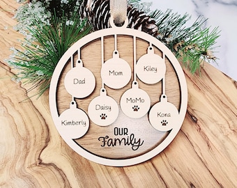 May include: A wooden Christmas ornament with the words "Our Family" in the center.  The ornament has seven smaller circles hanging from it, each with a name written on it: Dad, Mom, Kiley, Kimberly, Daisy, Momo, and Kona.  The circles for Momo and Kona have paw prints on them.