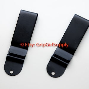May include: Two black metal belt clips with a rounded bottom and a small hole.  © Etsy: GripGirlSupply
