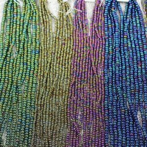 May include: Strands of iridescent seed beads in green, brown, purple, and blue. Each strand is labeled with a white tag indicating the color: Green Iris, Brown Iris, Purple Iris, and Blue Iris. The beads have a metallic sheen.