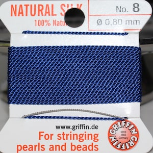 May include: A spool of natural silk thread in a deep blue hue, labeled "NATURAL SILK 100% Natural." The label indicates a diameter of 0.80 mm. Text on the label reads "For stringing pearls and beads" and includes the Griffin logo.