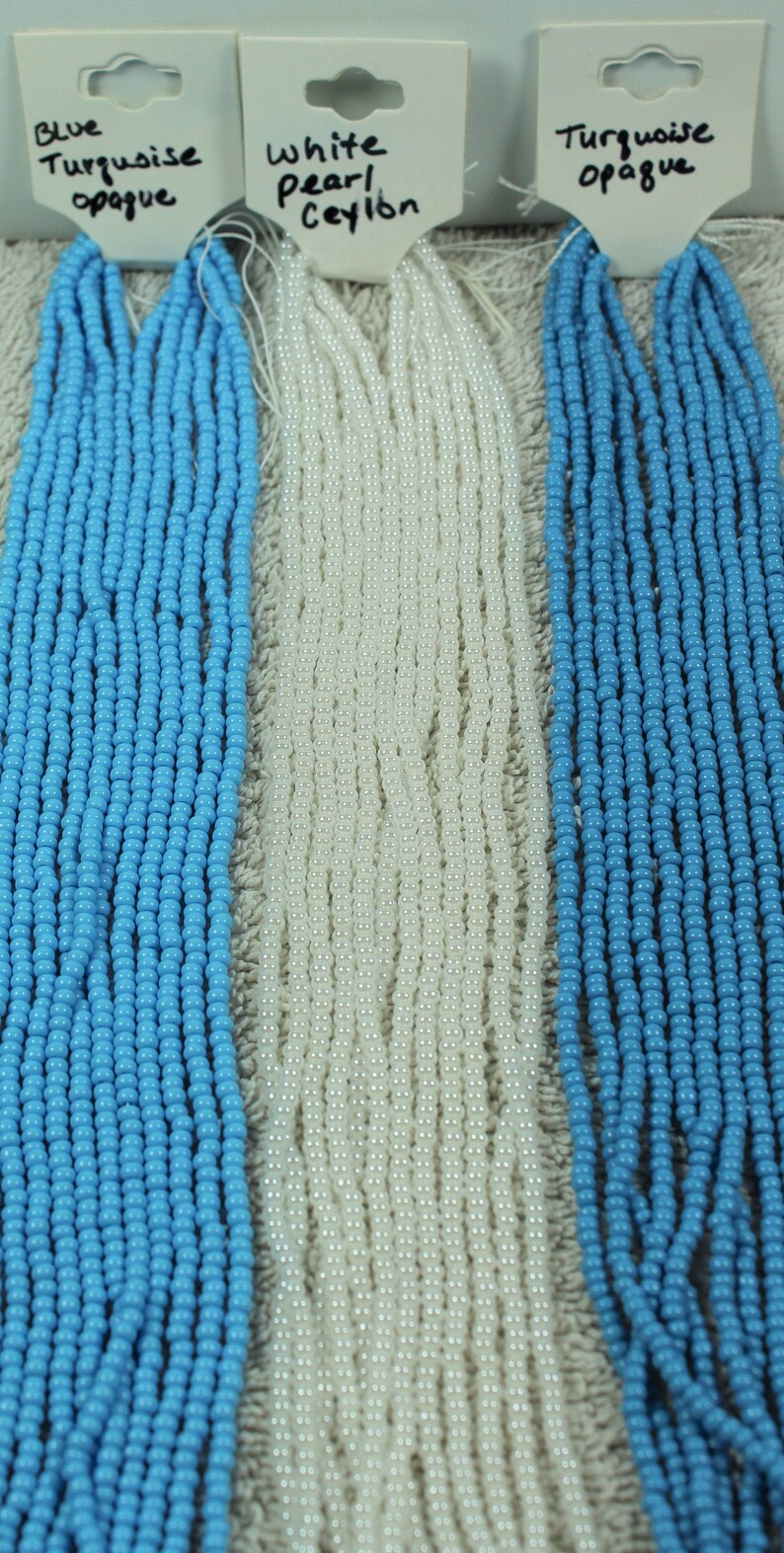 Peut inclure: Des fils de perles turquoises et blanches. Les &eacute;tiquettes indiquent "Blue Turquoise opaque", "White Pearl Ceylon" et "Turquoise opaque". Les perles rondes et petites sont parfaites pour la cr&eacute;ation de bijoux ou l'artisanat.