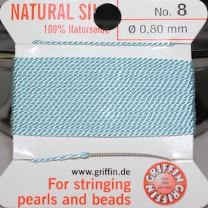 May include: A spool of light blue natural silk thread, labeled "No. 8" with a diameter of 0.80 mm. The packaging includes the text "For stringing pearls and beads" and the brand name "Griffin" since 1866.