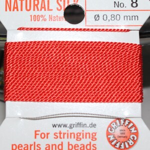 May include: A spool of vibrant red natural silk thread, labeled "NATURAL SILK" and "No. 8". The thread is 0.80 mm in diameter. The packaging includes the text "For stringing pearls and beads" and the brand name "GRIFFIN".