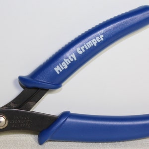 May include: A blue and black Mighty Crimper tool. The tool has blue handles with the words "Mighty Crimper" printed in white. The tool is designed for crimping wires and has a black metal head.