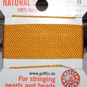 May include: A spool of golden-yellow Griffin Natural Silk thread, No. 8, for stringing pearls and beads. The label reads "100% Natural" and includes the website www.griffin.de and the Griffin logo, "since 1866 Germany."