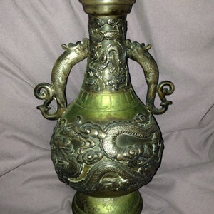 May include: An antique bronze vase with intricate dragon relief carvings. The vase features two dragon-shaped handles and a flared top. The bronze has a green patina, and the vase is approximately 12 inches tall.