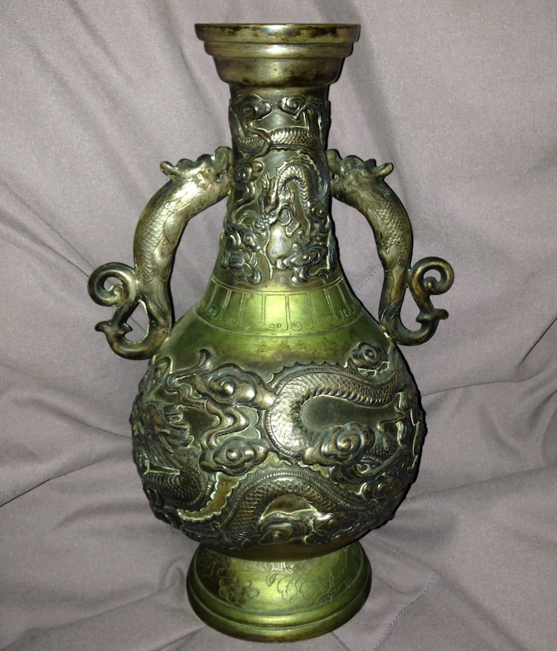 May include: An antique bronze vase with intricate dragon relief carvings. The vase features two dragon-shaped handles and a flared top. The bronze has a green patina, and the vase is approximately 12 inches tall.