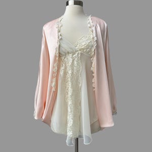 May include: A vintage lingerie set on a mannequin. The set includes a light pink satin robe with lace trim and a white slip with lace detailing. The lingerie is displayed against a gray background.