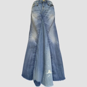 May include: A long denim skirt in shades of blue, featuring a flared, mermaid-style silhouette. The skirt has a classic five-pocket design, a button and zipper closure, and distressed detailing. The hemline is frayed, adding a casual touch to the garment.
