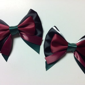 May include: Two black, burgundy, and green satin ribbon bows. The bows are tied in a classic style with the tails of the ribbon flowing down.