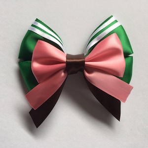 May include: A green, pink and brown bow with white stripes. The bow is made of satin ribbon and is tied in a knot.