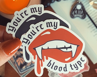 Könnte beinhalten: Ein weißer Aufkleber mit einem roten und schwarzen Vampirmund mit Zähnen und tropfendem Blut. Der Aufkleber lautet "You're my You're my blood type" in schwarzer gotischer Schrift.