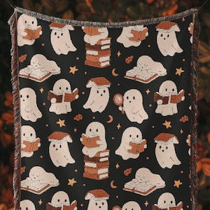May include: Black throw blanket with a repeating pattern of white ghosts reading books, stars, and moons. The ghosts are holding books or magnifying glasses. The blanket has a fringed edge and the text "Shadowbound Spines+" in a circle.