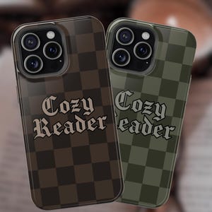 May include: Two phone cases with a checkerboard pattern. One case is brown, the other is olive green. Both cases have the words "Cozy Reader" in a gothic font. The cases are designed to fit a smartphone.