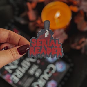 May include: A black and red sticker with the text "SERIAL READER" in dripping red letters. A bloody knife is depicted above the text.