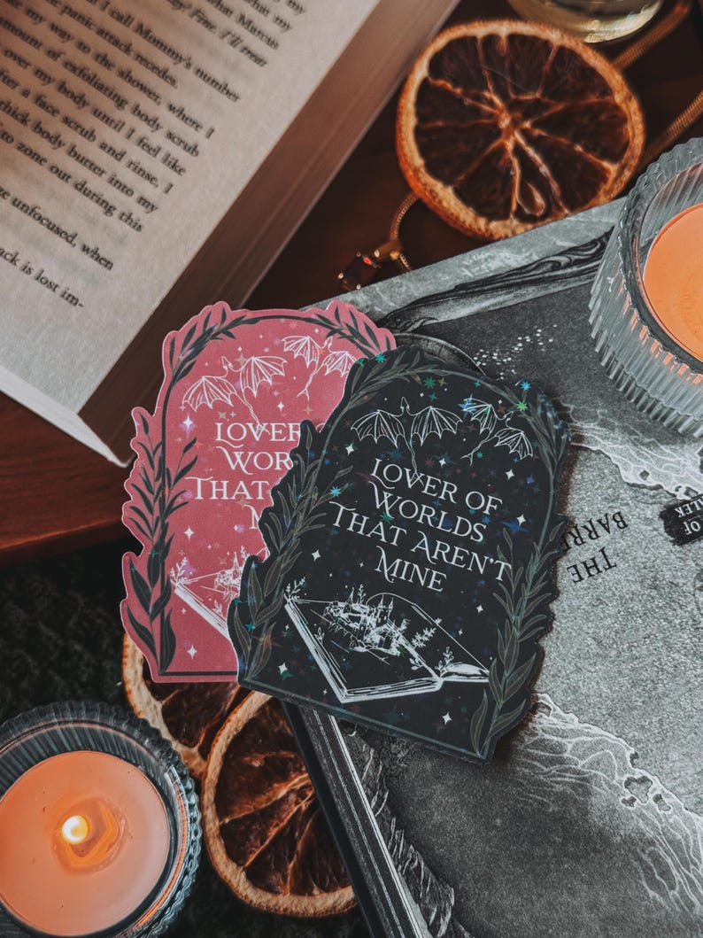 May include: Two black and pink stickers with a gothic aesthetic. The stickers feature a book with a forest scene and the text "Lover of Worlds That Aren't Mine".