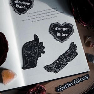 May include: Four black and white stickers with gothic-style text and imagery. The stickers feature the phrases "Shadow Daddy", "Dragon Rider", "Save a Dragon Ride a Shadow Daddy", and "Feral for Fantasy".