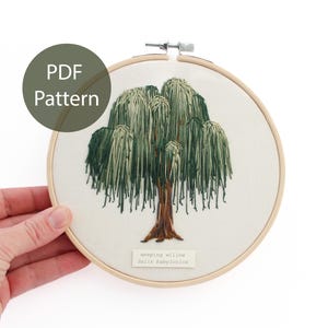 May include: Embroidered weeping willow tree in a wooden hoop. The tree features green and brown thread, with the text "weeping willow Salix babylonica" below the tree. A green circle with the text "PDF Pattern" is in the upper left.