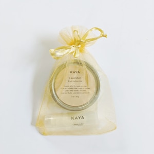 May include: A gold organza gift bag tied with a bow contains a round body lotion bar and a lip balm. The lotion bar is in a silver tin with the text "KAYA Lavender Body Lotion Bar". The lip balm also has the text "KAYA Lavender".