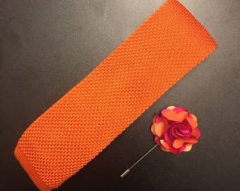 May include: Orange knitted tie with a matching orange and pink flower lapel pin.