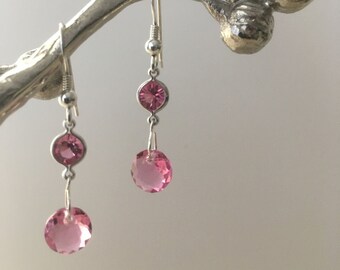 May include: A pair of silver dangle earrings with pink crystal drops. The earrings feature a smaller pink crystal above a larger pink crystal.