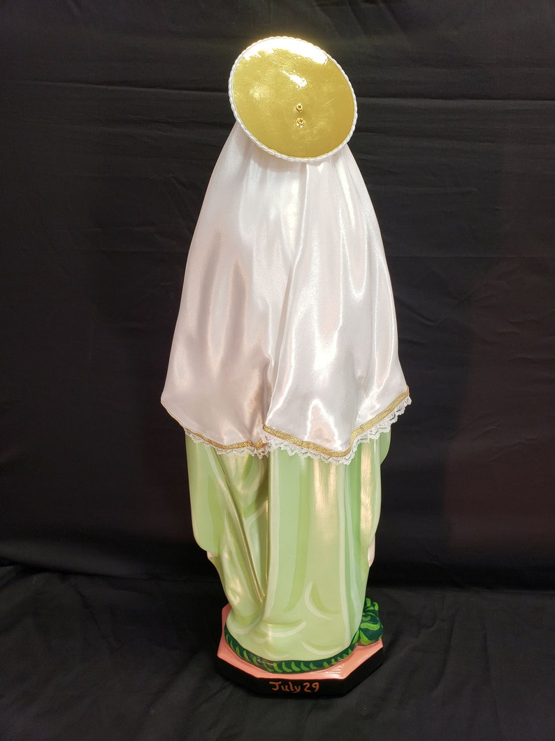 Pu&ograve; includere: Statua religiosa di una figura che indossa un velo di raso bianco e un'aureola dorata. La veste della figura &egrave; verde chiaro con accenti dorati. La base &egrave; nera con la scritta "July 29".