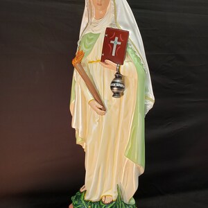 Pu&ograve; includere: Statua di Santa Marta, raffigurata in abiti fluenti con un'aureola. Tiene in mano una torcia e un libro con una croce, e si erge su un drago verde. La base &egrave; incisa con "Saint Martha".