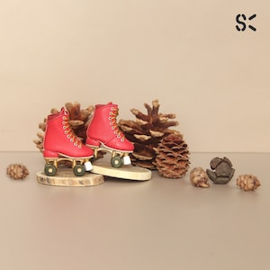 May include: A pair of red roller skates with gold wheels and white wheels. The skates are on a wooden surface with pine cones around them.