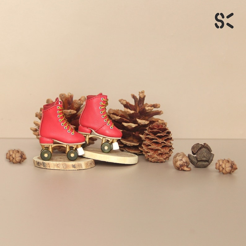 May include: A pair of red roller skates with gold wheels and white wheels. The skates are on a wooden surface with pine cones around them.