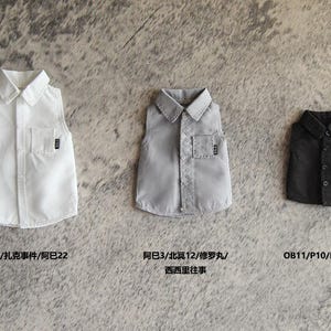 May include: Three sleeveless shirts in white, grey, and black, each with a chest pocket and a small label. The shirts are displayed on a textured, neutral surface. Text is visible below each shirt.