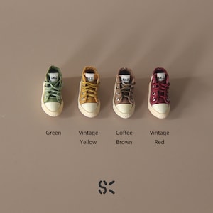 May include: Four miniature canvas high-top sneakers in different colors: green, yellow, brown, and red. Each shoe has the text "SKC" on the side.