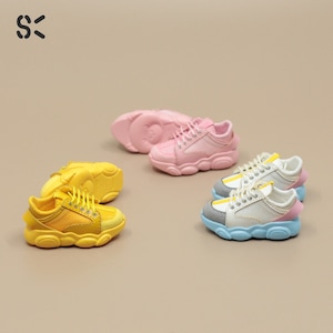 May include: Three pairs of colorful sneakers with chunky soles. The sneakers are in pink, yellow, and white with gray accents. The sneakers have mesh panels and laces.