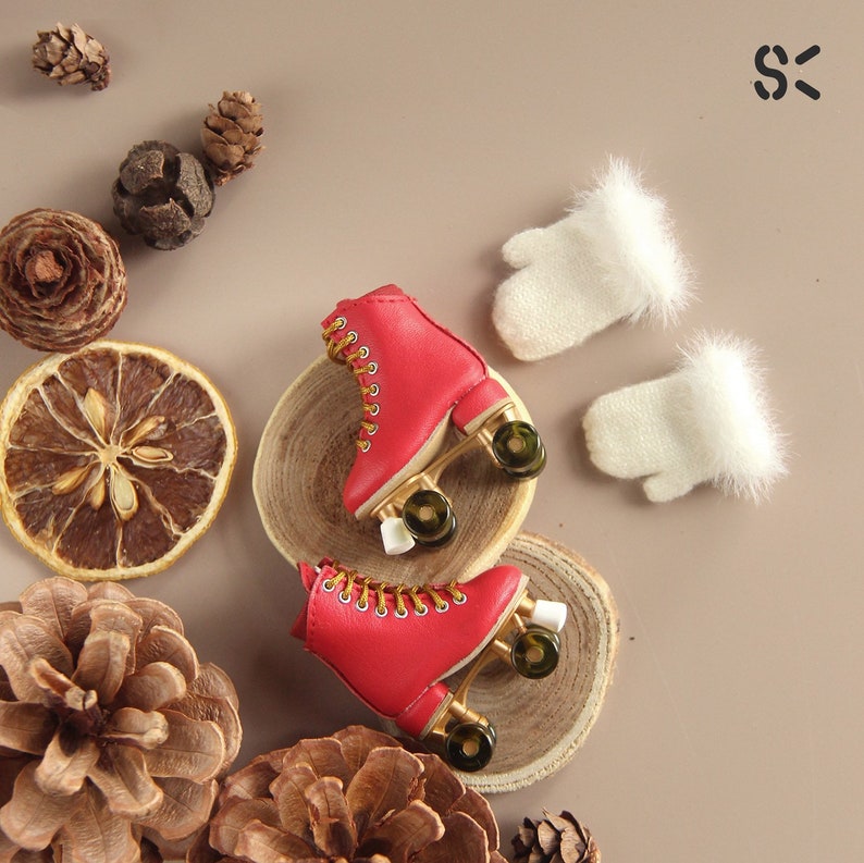 May include: Two pairs of red roller skates with gold wheels and white fur trim. The skates are on a wooden surface with pine cones and dried citrus fruit.