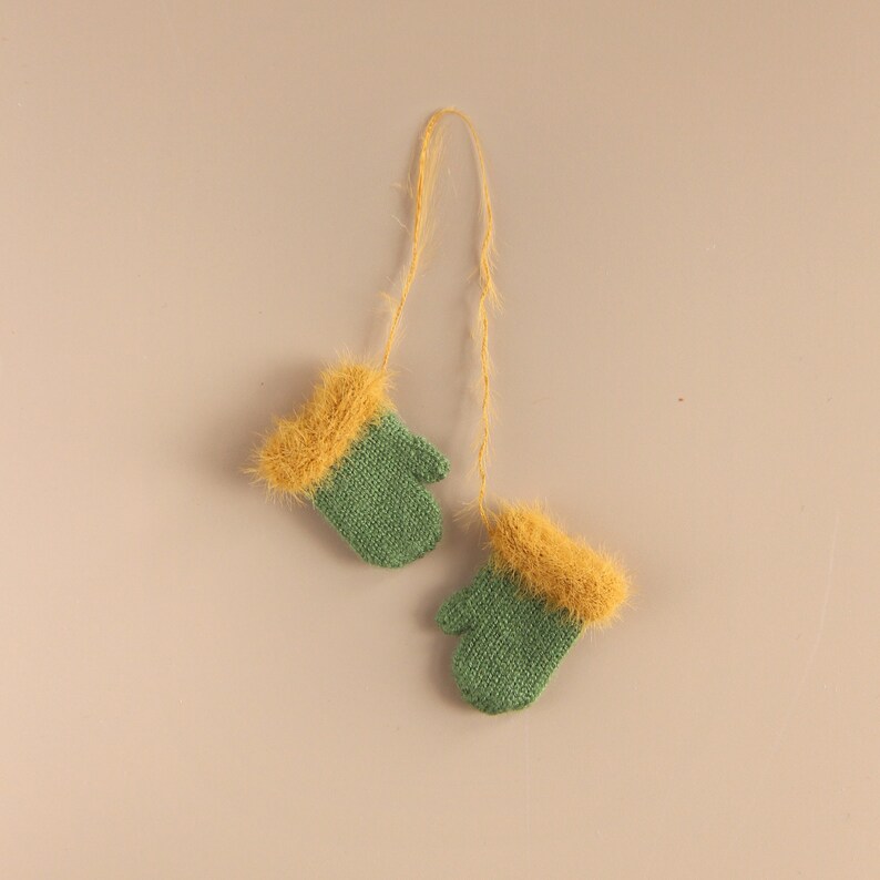 May include: A pair of green knitted mittens with yellow fuzzy trim, connected by a string.