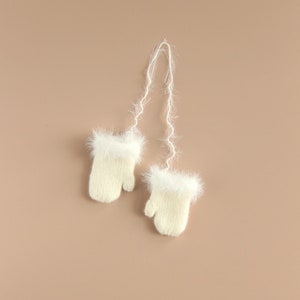 May include: A pair of white knitted mittens with fluffy white trim and a long white string attached.
