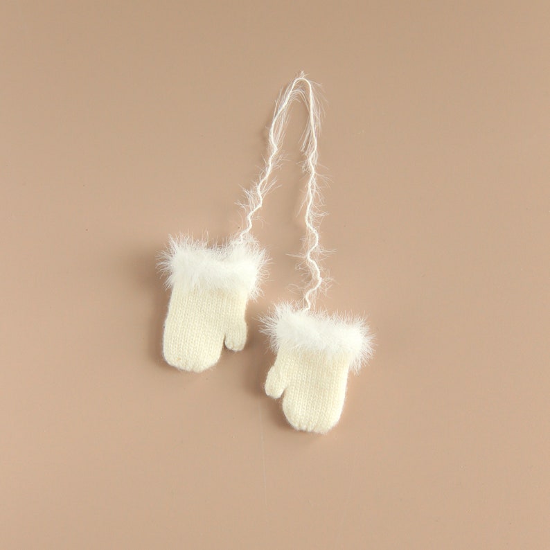 May include: A pair of white knitted mittens with fluffy white trim and a long white string attached.