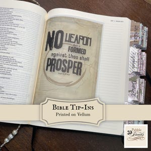 May include: An open Bible featuring a translucent vellum tip-in page with the black text No Weapon That Is Formed Against Thee Shall Prosper Isaiah 54:17 KJV. The page has a vintage map background and decorative book tabs on the right edge.