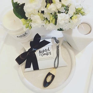 May include: A white box with a black ribbon and the text "Addicted to Candles" with the scent "Lemongrass & Persian Lime". A wooden diffuser with a black cap is hanging from a black and white cord.