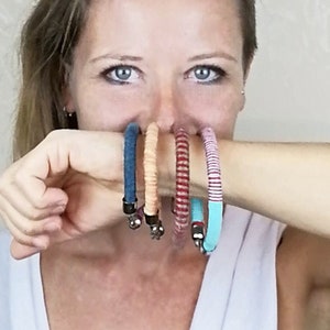 May include: A woman is wearing four colourful bracelets on her wrist. The bracelets are made of fabric and have a variety of patterns. The bracelets are stacked on top of each other, with the blue bracelet at the bottom and the turquoise bracelet at the top.