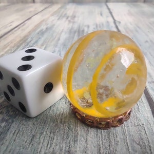 May include: A white dice with black dots and a clear glass marble with a yellow swirl design.