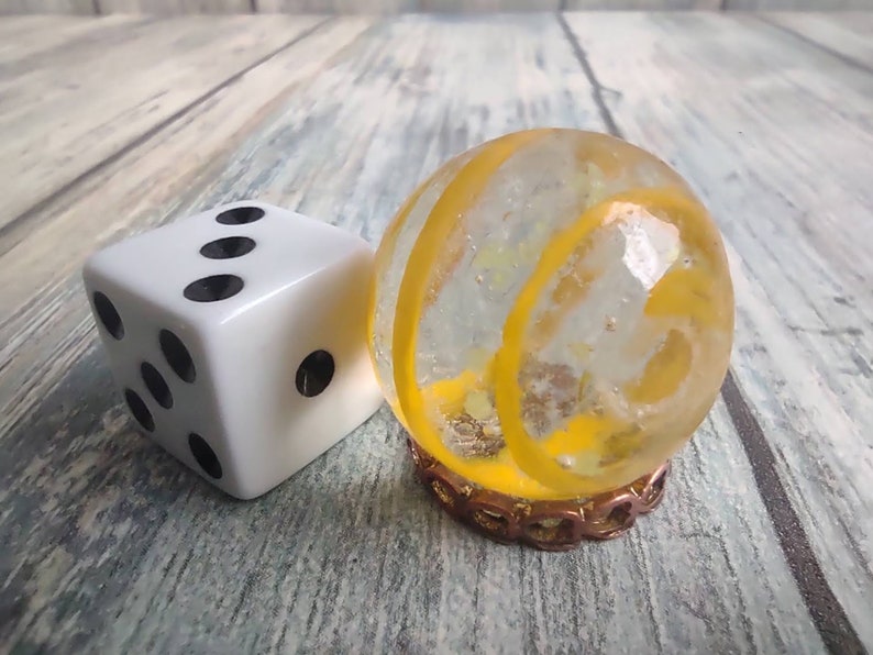 May include: A white dice with black dots and a clear glass marble with a yellow swirl design.