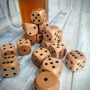 May include: A group of wooden dice with black dots on each side. The dice are stacked in a pyramid shape on a light blue wooden surface. A glass of beer is in the background.