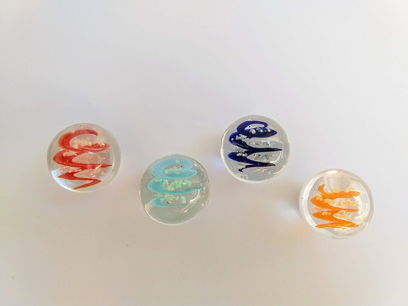 May include: Four glass marbles with swirling patterns inside. The marbles are clear with red, blue, turquoise, and orange swirls.