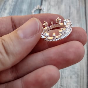 May include: A silver ring with a crown design. The ring is set with small, clear stones.