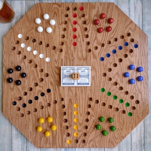 May include: A wooden game board with a hexagonal shape and a variety of colored marbles. The board has a central area with two dice and the words "Determinations" and "Plastic Dice".