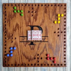 May include: A wooden game board with a personalized inscription "Palmer" and a deck of playing cards. The board has a grid of holes and is decorated with colorful marbles.